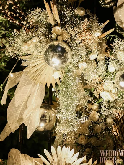 A detailed shot of the floral installation, showing the mix of shimmering silver balls, delicate baby's breath, and dried, painted leaves. It's a symphony of textures.