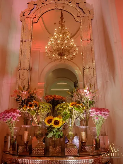 An ornate mirror and a grand chandelier create a perfect frame for a symphony of sunflowers and pink chrysanthemums, blending grand elegance with a touch of rustic charm.