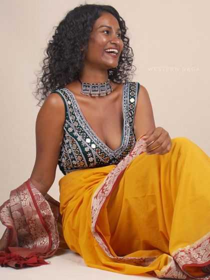 A lifestyle-oriented shot of the model styled in the green blouse and yellow saree. Her joyful expression and relaxed pose create an aspirational mood for the brand.