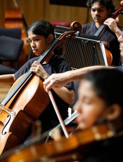 A close-up on the cello section during a rehearsal, showing the focus and determination of our students as they play alongside seasoned professionals. This is where musical growth accelerates.