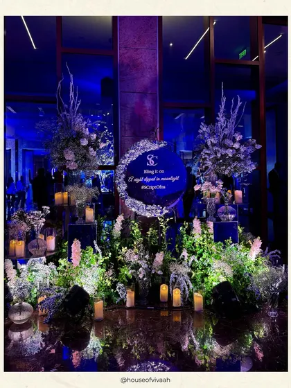 A custom monogrammed sign for the couple, nestled in a bed of white florals and surrounded by candles, creating a personalized and romantic welcome to their galaxy-themed Sangeet.