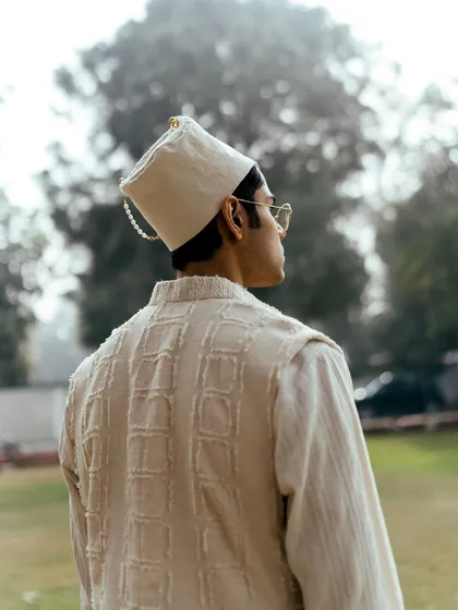 A back profile shot for Sanchit Sharma, highlighting the texture of the vest and the unique design of the hat. The soft, diffused background keeps the focus on the clothing.