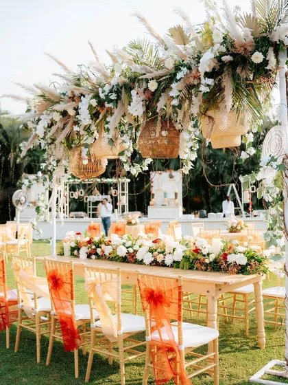 We transform outdoor spaces into breathtaking venues for daytime celebrations. This long table setup features a lush overhead floral canopy with rustic wicker lanterns, creating a beautiful and intimate dining experience for guests.