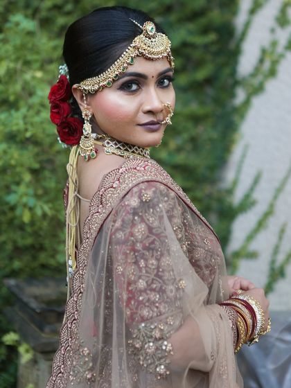 A beautiful side profile showing the elegant bridal bun adorned with red roses and the flawless makeup.