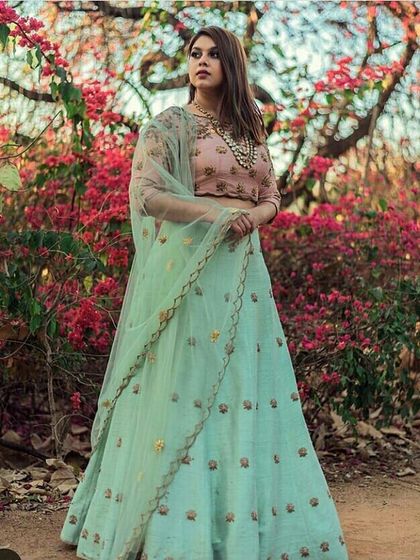 A model wearing a beautiful mint green lehenga with a contrasting blush pink blouse. The delicate floral embroidery on the skirt makes this a subtle and sophisticated choice for a summer wedding.