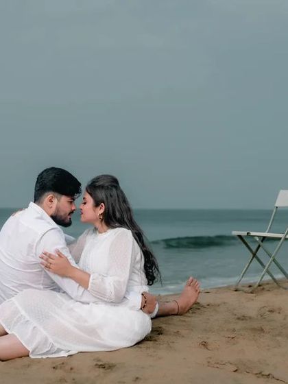 An intimate moment on a quiet beach, with the couple sitting on the sand. The two empty chairs suggest a story of a world that is just for them.