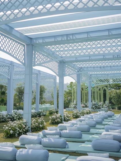 The guest seating area under the white lattice pergola, with low floor seating and cushions in pastel blue, creating a serene and modern look.