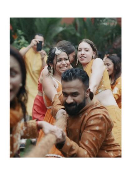 Friends and family playfully hold back the bride during a fun moment at the Haldi, capturing the community and laughter.