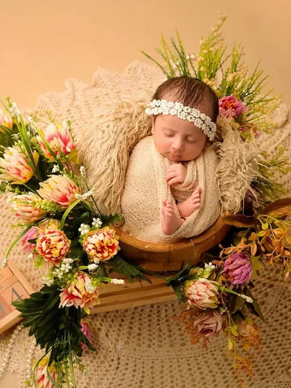 An overhead view of a beautiful newborn setup. The baby is nestled in a wooden prop, surrounded by flowers and placed on a delicate lace blanket, creating a rich, textured portrait.