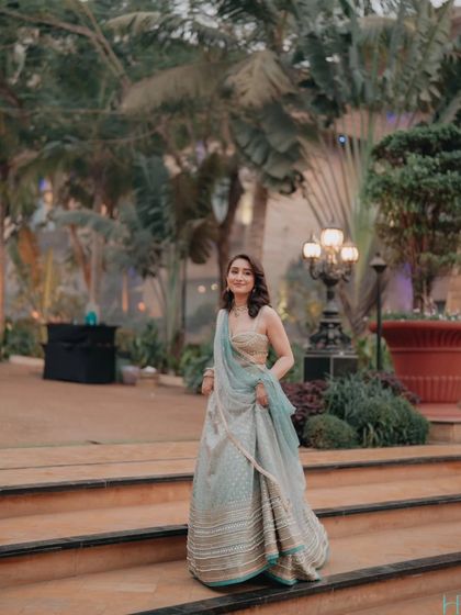 A full-length shot of the bride walking down a set of stairs in a garden, her light blue lehenga flowing gracefully.