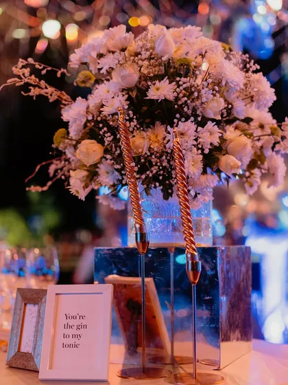 A charming detail from a Sangeet tablescape. A cute, framed quote, "You're the gin to my tonic," sits beside elegant spiral candles and a fresh white floral arrangement, adding a personal and playful touch.