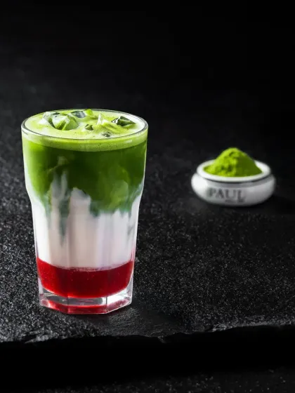 A layered iced beverage with a red strawberry base, milk, and a green matcha top.