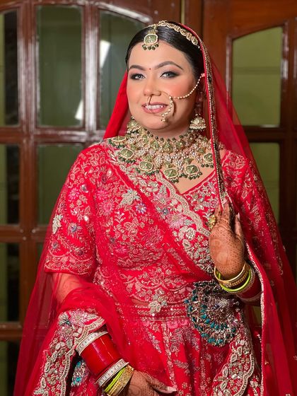 A beautiful portrait of a bride in a traditional red lehenga, her smile lighting up her face. The makeup is classic and elegant.