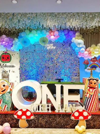 A vibrant and playful Cocomelon themed first birthday party. This full stage setup is packed with character cutouts, a massive rainbow balloon arch over a sparkling backdrop, and large "ONE" marquee letters, ready for a day of fun.