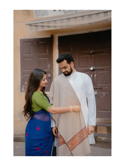 An intimate moment of care and affection, as the bride adjusts the groom's shawl in a quiet city corner.