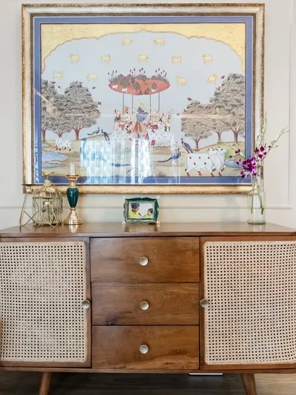 A close-up of a vintage-inspired wooden console with rattan doors. The piece is topped with a beautiful traditional Indian painting, creating a corner that is rich in culture and craftsmanship.