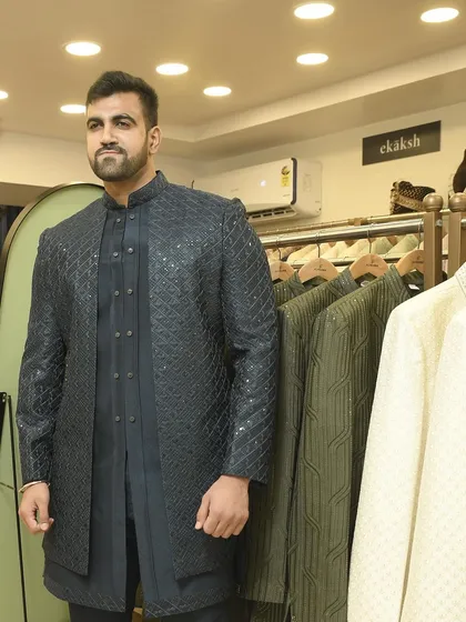 A customer trying on the black textured Indo-western jacket in our store, surrounded by more of our extensive collection.