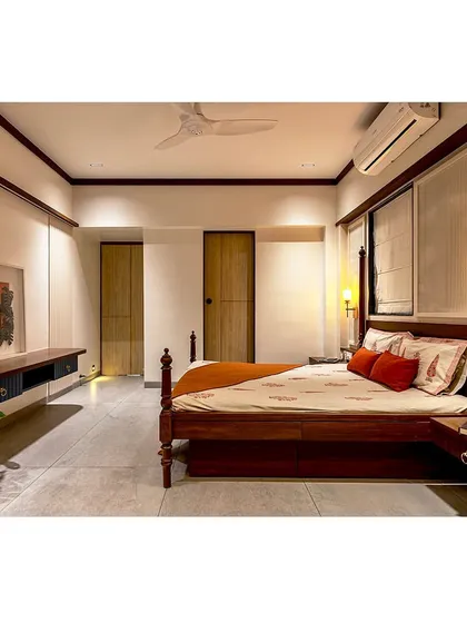 A master bedroom designed with a warm, rustic-modern aesthetic. The four-poster bed is made from rich, dark wood, complemented by a deep peacock blue wardrobe and rust-orange accents.