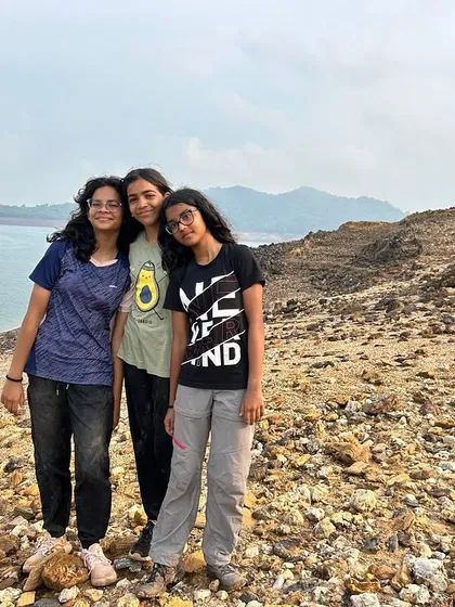 Three friends pose for a photo on the rocky shore, memories made during their adventure camp.