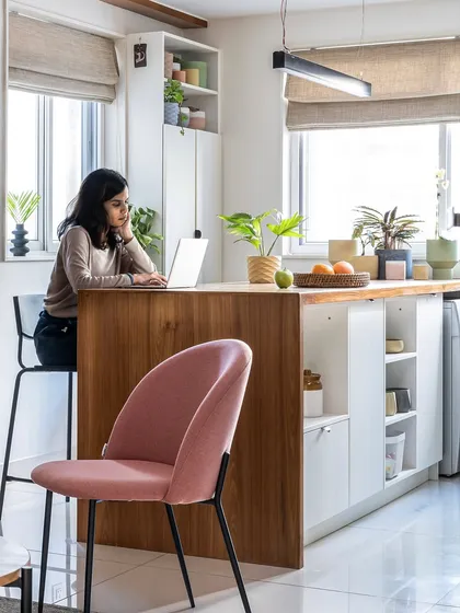 The multifunctional kitchen island in the 'Footloose' project serves as a workspace, dining spot, and storage hub. It features a warm wood finish and integrates seamlessly with the white cabinetry.