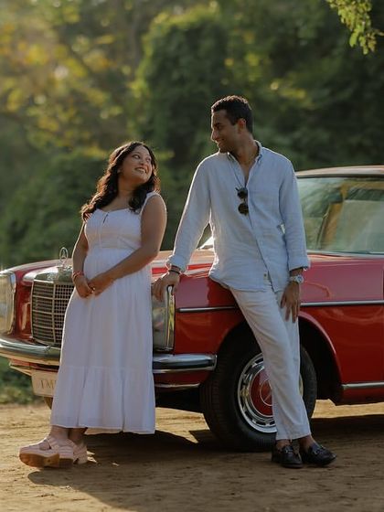 This image, similar to a previous one, showcases the couple's relaxed chemistry. Leaning against the classic car, they share a look that is both candid and full of affection, perfect for a lifestyle couple shoot.