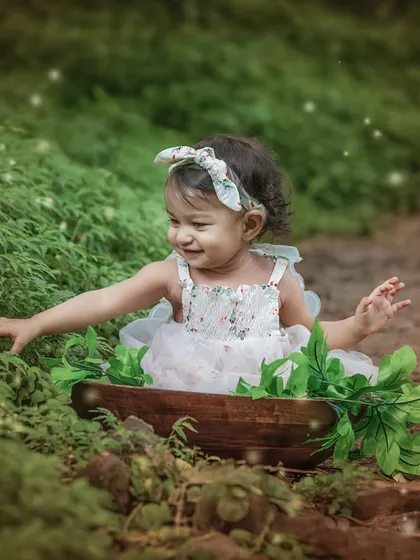 A happy baby reaches out to touch the surrounding greenery, her smile as bright as the magical sparkles of light around her.