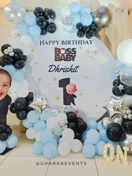 A cute Boss Baby first birthday with a personalized touch. The circular backdrop includes a photo of the birthday boy alongside the Boss Baby character, framed by a blue, black, and white balloon arch.