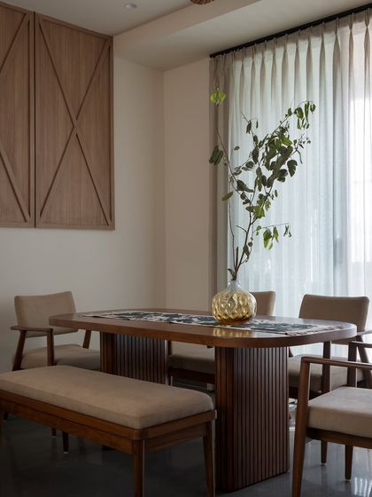 A wider view of the dining space, showing its connection to the living area. Daylight filters in through sheer curtains, creating a bright and open atmosphere for shared meals.
