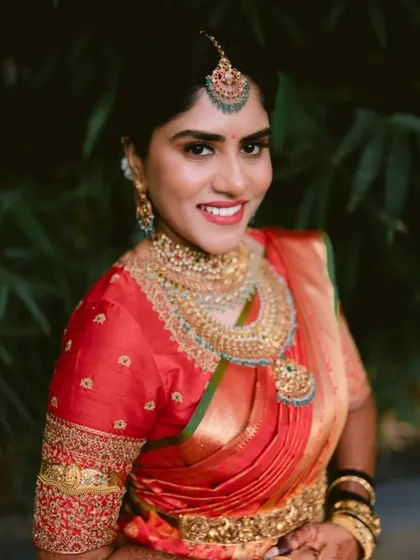 A bride in a classic red Kanchipuram saree. Her custom red blouse is adorned with heavy gold embroidery on the sleeves, a timeless choice for a muhurtham look.