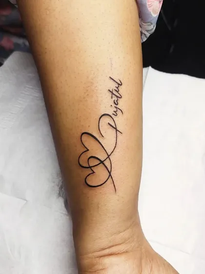 A name tattoo, 'Pujatul', integrated with two intertwined hearts. This design beautifully combines a name with a symbol of love.