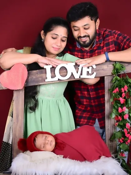 A loving family portrait with parents admiring their newborn baby in a "love" themed setup.