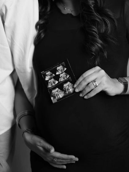 A close-up detail shot in black and white. The mother holds the sonogram against her bump, a powerful image that connects her baby's first picture to where they are growing safely.