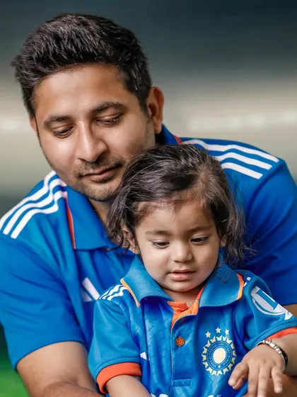 A tender moment between father and son, both in matching jerseys, examining the cricket bat. These quiet, candid shots are just as powerful as the action poses.