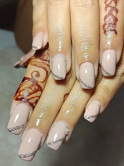Nude bridal nails with a touch of glam. This design combines a neutral base with delicate silver glitter and pearl details for a look that is pure class.