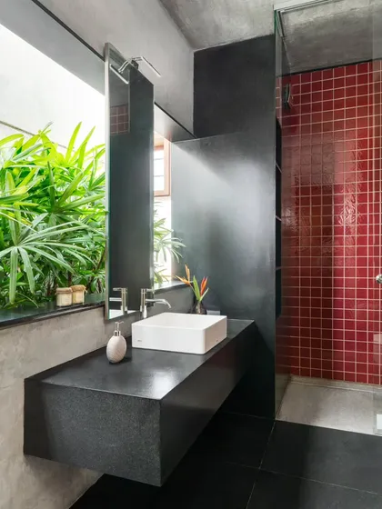 Even private spaces are an opportunity for design excellence. In The Quarry House, this bathroom opens to a private green space, blending raw materials like black stone and red mosaic tiles with natural light to create a sanctuary that feels like a personal resort.