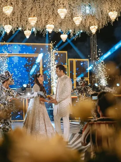 The couple's grand entrance to the Sangeet stage, surrounded by performers and pyrotechnics.
