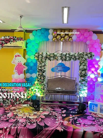 This hall decoration for a baby shower features two different arches, one with flowers and one with balloons, creating a layered and dynamic look. A decorated jhula sits at the center, ready for the ceremony.