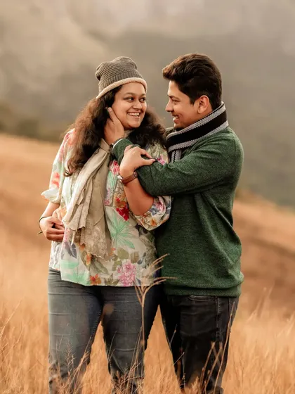 An intimate and cozy pre-wedding portrait of a couple in warm winter clothing, sharing a hug in a field of dry grass.