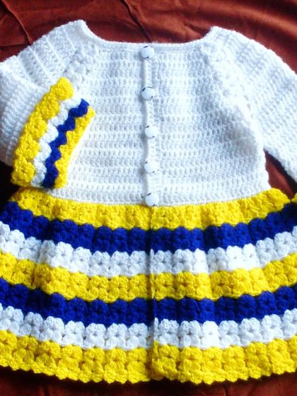 A bold and bright baby cardigan with stripes of yellow, blue, and white. This cheerful sweater is sure to stand out and bring a little sunshine to any day.
