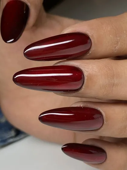 A stunning deep crimson polish on long, almond-shaped nails. The rich, glossy color is dramatic and elegant.