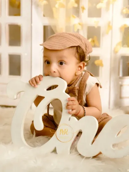 A baby boy celebrating his first birthday with a boho-themed shoot, chewing on a large "One" sign.
