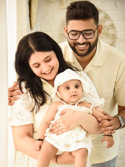 A happy family portrait celebrating their baby's six-month milestone. The coordinated light-colored outfits and bright setting create a fresh and airy feel.