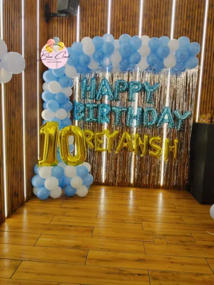 A blue and white balloon arch with 'Happy Birthday' foil letters for a 10th birthday celebration at home.