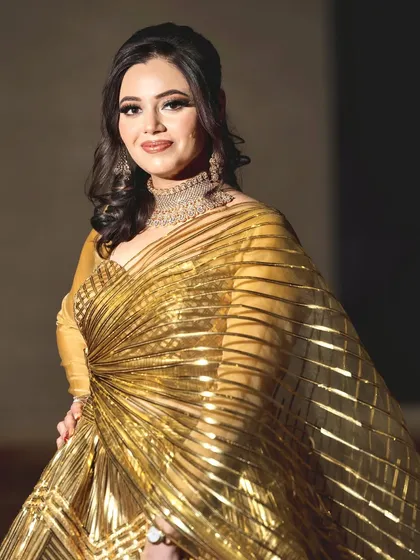 A stunning sangeet bride in a metallic gold gown. The makeup is equally glamorous, with a smokey eye and a radiant finish to match the opulence of her outfit.