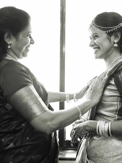 A happy, black and white shot of a mother helping her daughter get ready for her South Indian wedding.