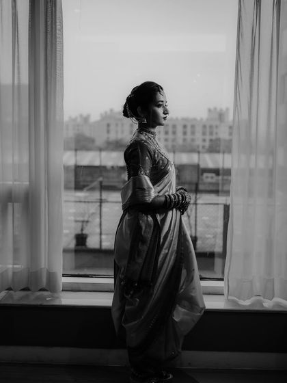 A stunning black and white silhouette of the bride standing by a window, creating a dramatic and contemplative bridal portrait.