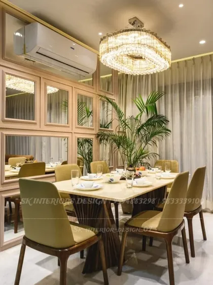 A luxurious dining setting featuring a large crystal chandelier as the centerpiece. The wall is paneled with mirrors, reflecting light and creating an expansive feel, while a large indoor plant adds a touch of nature.