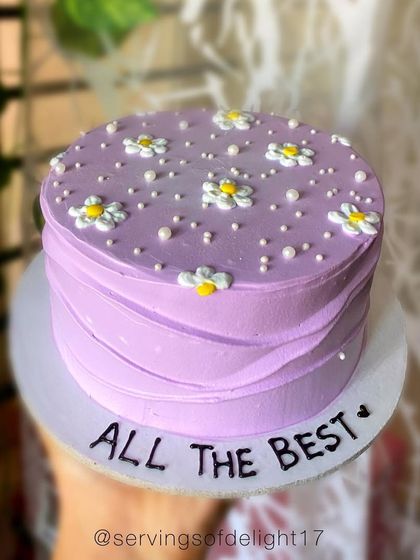 A simple yet pretty lavender cake with piped daisies, sending a message of "All The Best" for a new venture or exam.