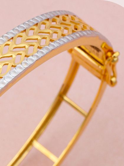 A wide gold kada with an intricate, geometric latticework pattern, accented with a rhodium-plated border. This is a bold, statement piece that showcases our skill in creating detailed designs.