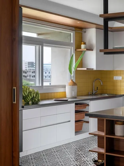 This view of the 'Vasudhalayah' kitchen shows how the sliding doors open up the space to the dining area. The design includes handleless white cabinets and convenient pull-out baskets.